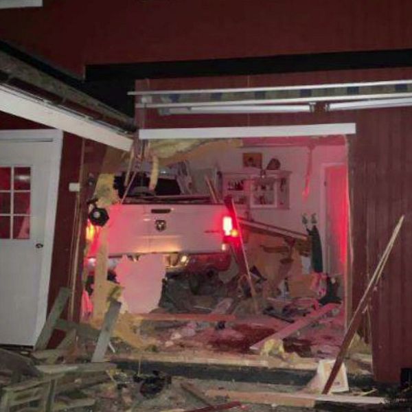 Till vänster syns en person som intervjuas, med en stadsmiljö i bakgrunden. Till höger visas en bild av en bil som har kört in i en byggnad och orsakat omfattande skador, med träplankor och inredning som är förstörda.