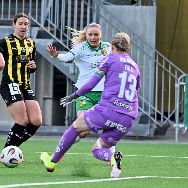 Fotbollsmålvakt i lila räddar skott mot två backar i svartgula tröjor och en anfallare.