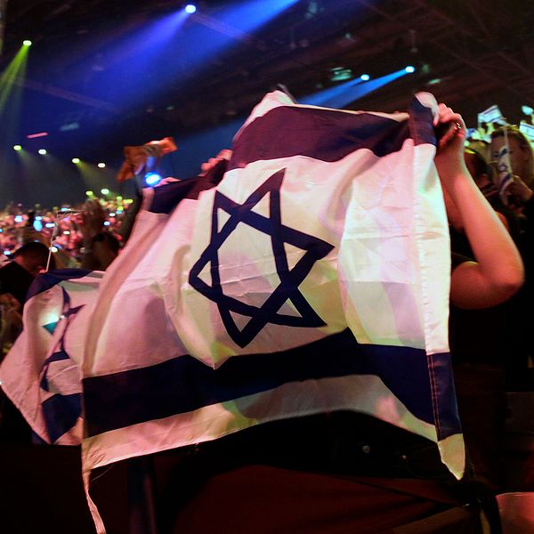 Den israeliske Eurovision-experten och tidigare talesmannen 2019för Israels Eurovision-delegation Alon Ami tillsammans med en bild på Israels flagga från Eurovision