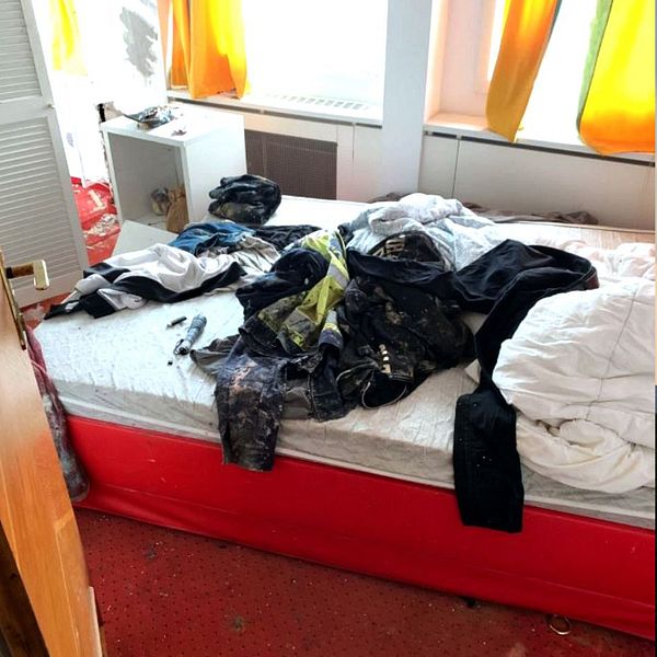 Rörigt rum med skräp och kläder utspridda. Vänster sektion visar en skräpkorg och ett skrivbord med tomma flaskor och en stol. Höger sektion visar en säng med en ostädad sängkläder och kläder som ligger utspridda på golvet.