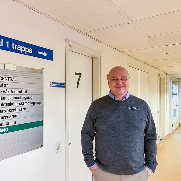 En man i grå tröja står vid en vägg i en korridor på vårdcentralen i Årjäng.