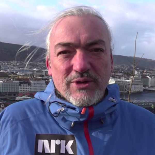 Husbyggnader som står i vatten som stigit och en närbild på en NRK-reporter.