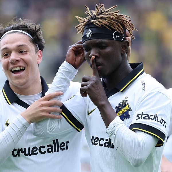 AIK:s Zadok Yohanna i vit matchtröja under intervju med lagkamrat i bakgrunden