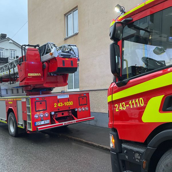 En delad bild som visar två sektioner. Den vänstra sektionen visar en person i en grå tröja med en keps, på en gata med flerbyggnader i bakgrunden. Den högra sektionen visar en röd brandbil med en uppfällbar stege, parkerad vid en byggnad. Text på brandbilen visar identifieringsnummer.