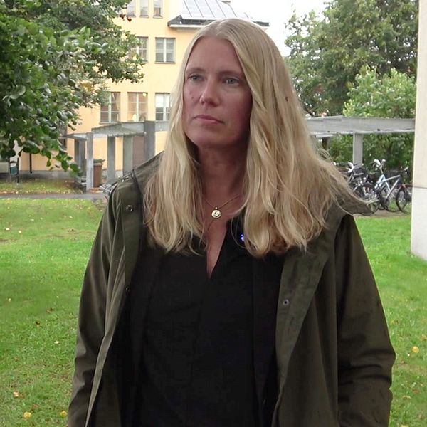 En kvinna står på en gräsmatta framför ett träd