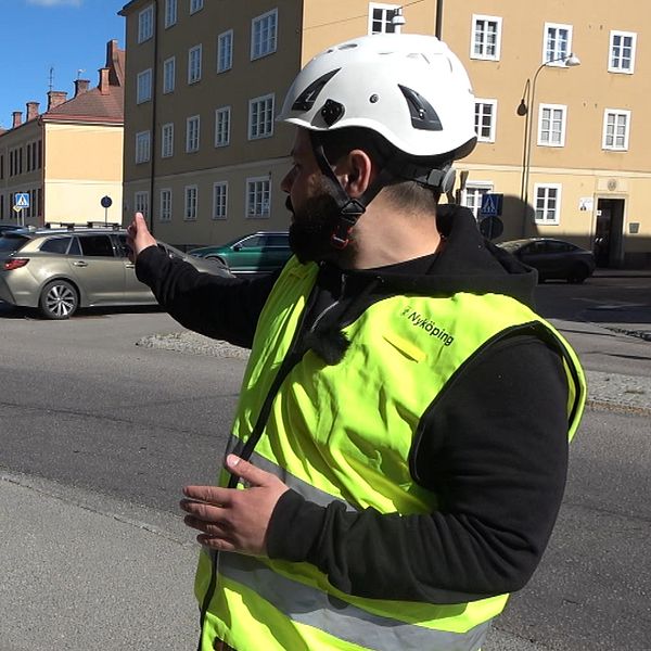 Person i reflexväst och hjälm pekar ut mot en korsning vid ett bostadshus.