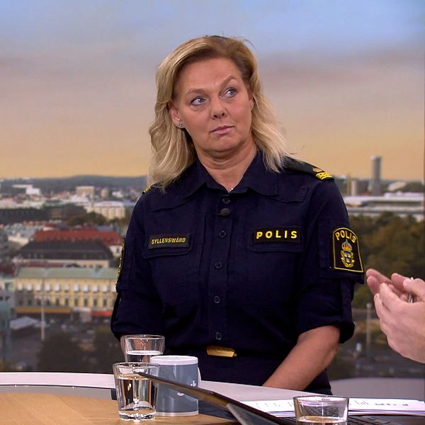 Två personer i poliskläder sitter vid ett bord i en studio under en intervju.