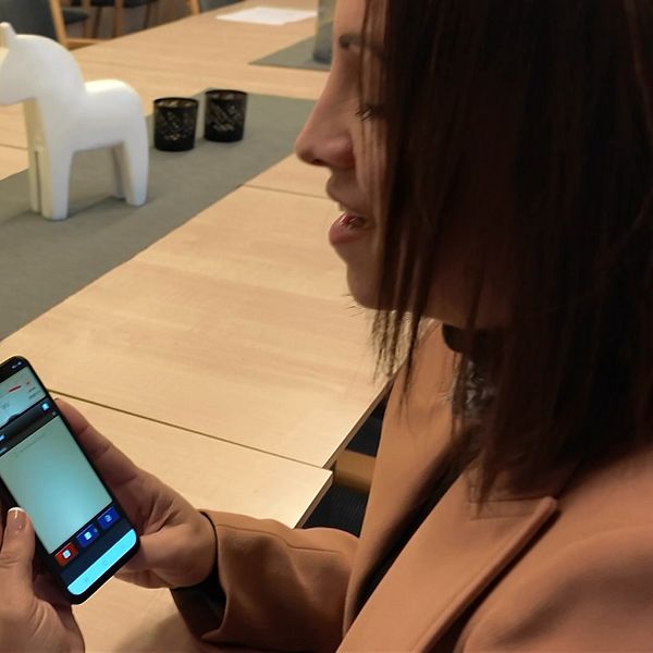 En person sitter vid ett konferensbord och talar i en smartphone.