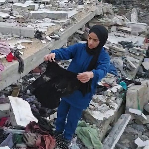 Kvinna granskar kläder vid ruiner i Gaza.