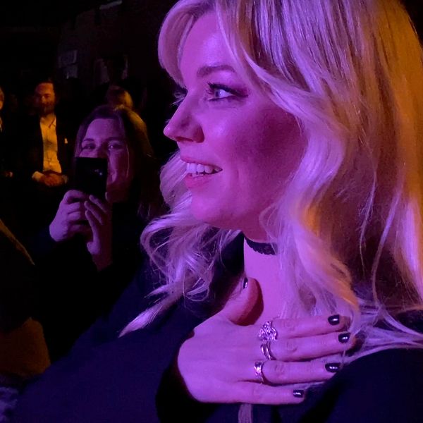 en blond kvinna som ler och håller sig över bröstet. i ett publikhav.