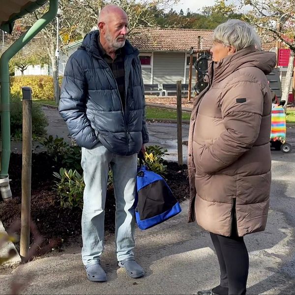 En delad bild som visar en övervakningskamera monterad på en hög stolpe i vänstra sektionen, och i den högra sektionen står en person i en grå jacka och samtalar med en kvinna i en brun ytterjacka. I bakgrunden syns en grön bänk och en trädgårdsmiljö med buskar och blommor.