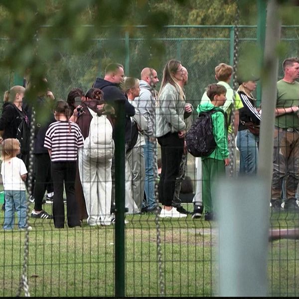 Personer samlas bakom stängsel vid en plats med polisavspärrning efter en attack.
