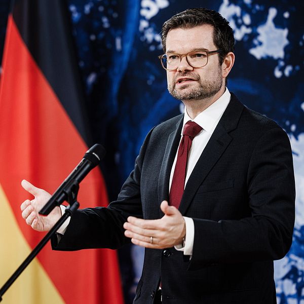 En man står upp och talar i en mikrofon framför Tysklands och EU:s flagga.