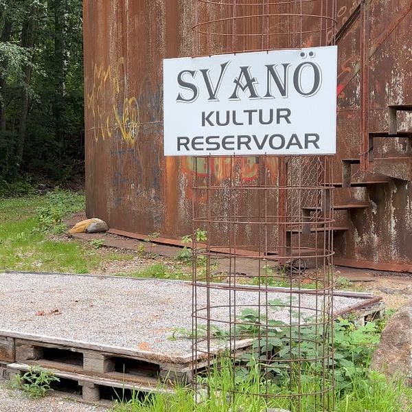 Svanö resvoar-skylt framför cisternområdet. Med tre ordförande för Svanö-föreningar som kommer gåendes mot kameran.