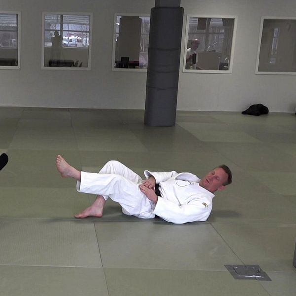 Två personer i judodräkter övar tekniker på en träningsmatta i en dojo.