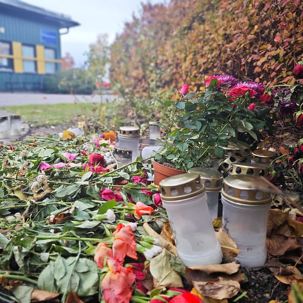 Minnesplats med ljuslyktor och blommor på marken