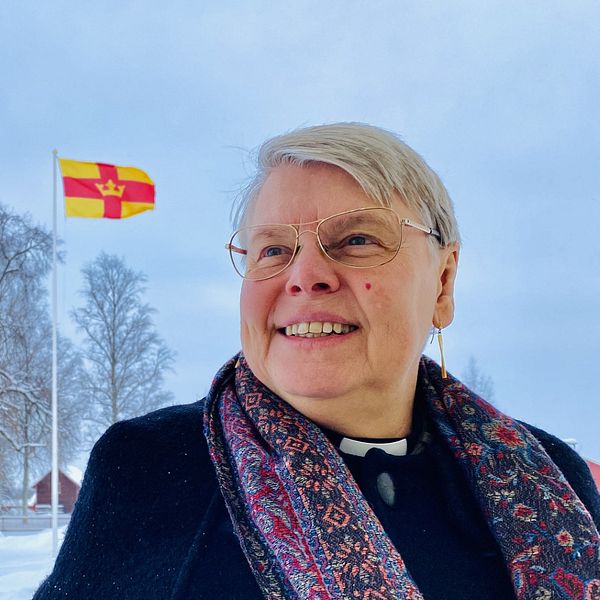 Präst i Gagnef och tittar mot himlen, med Svenska kyrkans flagga i bakgrunden.