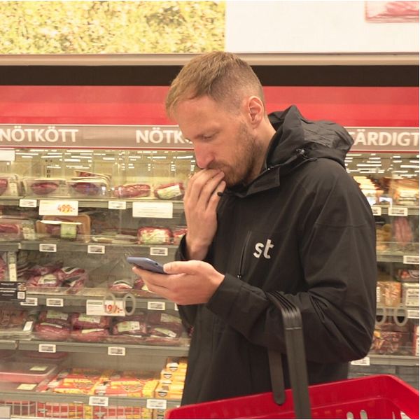 Varor i en mataffär. Man tittar på sin telefon.