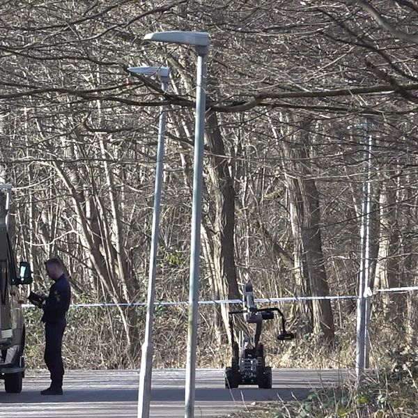 Polis vid skåpbil och robot i skogsmiljö.
