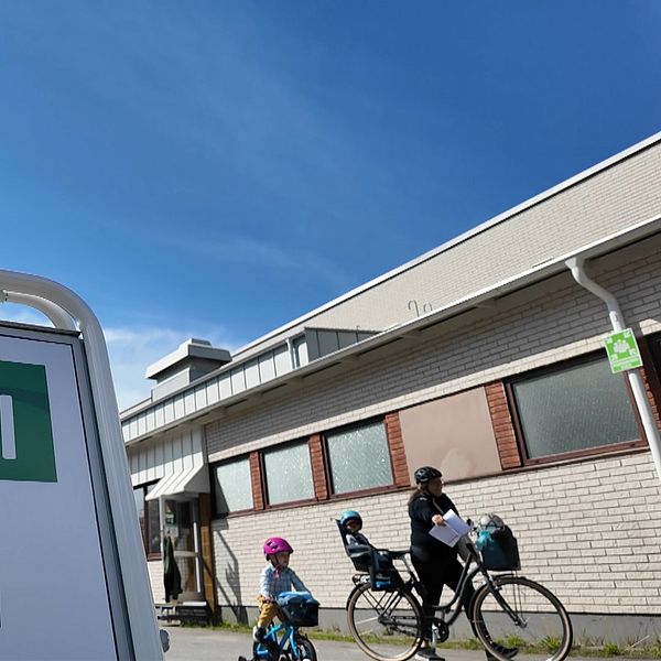 Vallokalsskylt och familj med cyklar i bakgrunden.