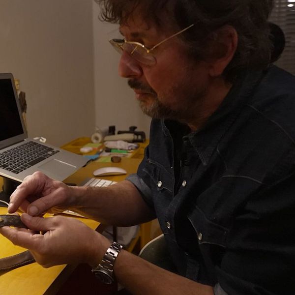 Nära bild på ett hundhalsband med datummärkning. Dennis Dahlqvist sitter vid ett bord och pekar mot halsbandet.