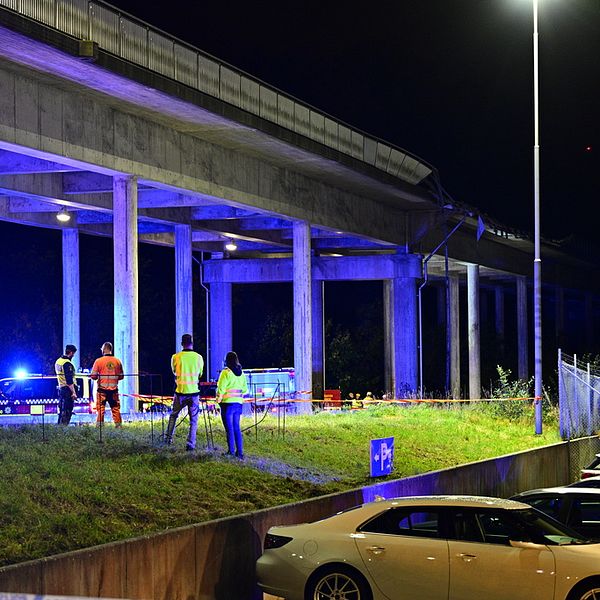 Blåljusfordon och personer i reflexkläder står under en betongbro.