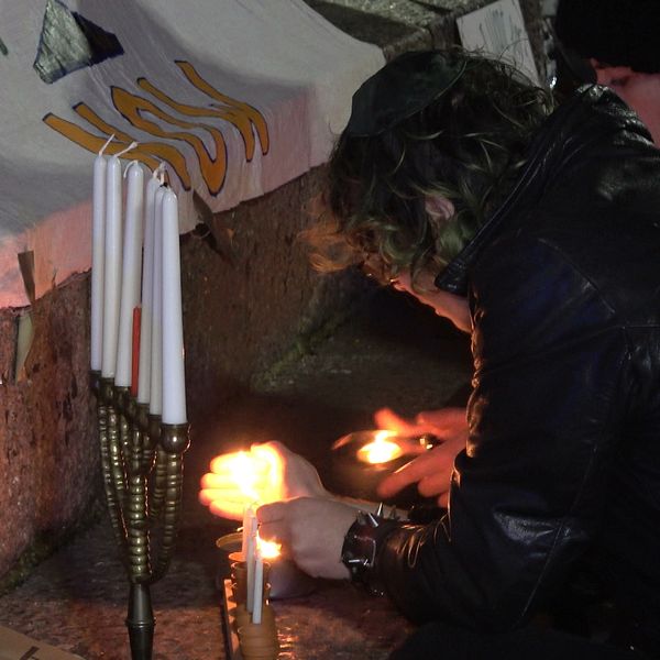 Elias Gordon tänder ljus i en ljusstake under en manifestation i Malmö. På en skylt står det ”vapenvila, fred”