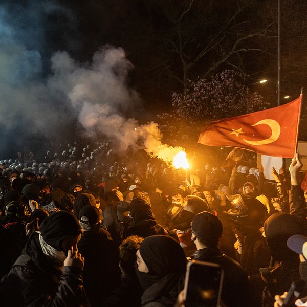 Folkmassa protesterar med turkisk flagga och facklor, rök fyller natthimlen.