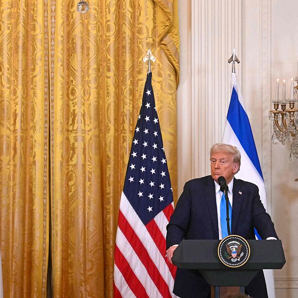Netanyahu och Trump står på ett podium framför amerikanska och israeliska flaggor i en officiell presskonferens. De är inomhus med en guldfärgad gardin i bakgrunden.