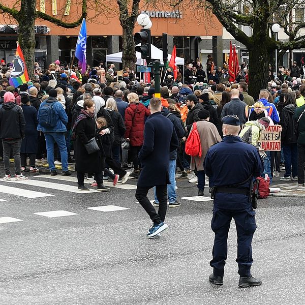 En kvinna framför en mikrofon och flera personer på plats på ett torg