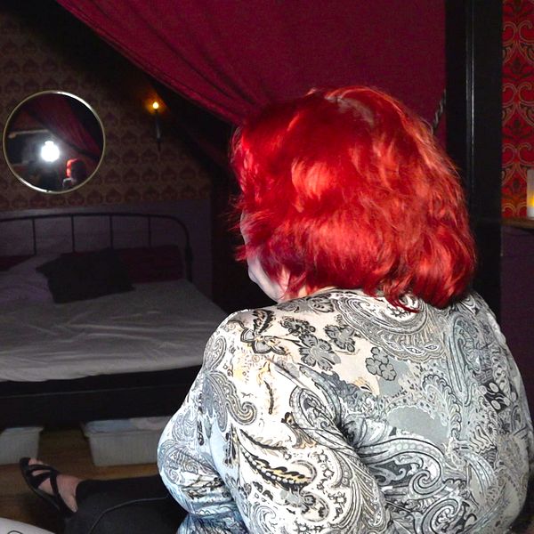 Arrangör till swingersklubb sitter på säng tillsammans med annan besökare med mask på.