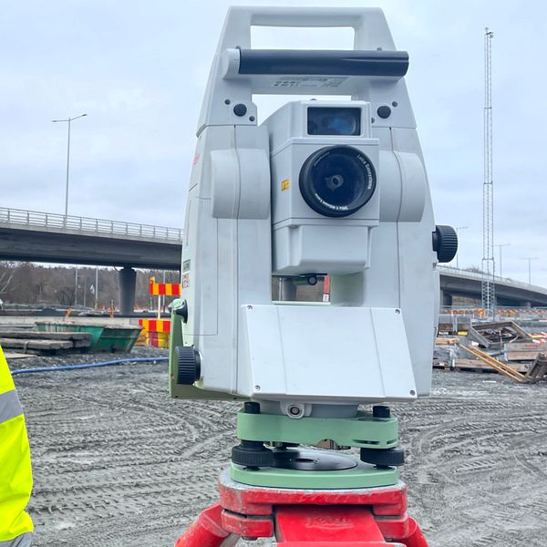 Mätchef Sebastian Andersén i varseljacka och hjälm bredvid en totalstation på byggarbetsplats.