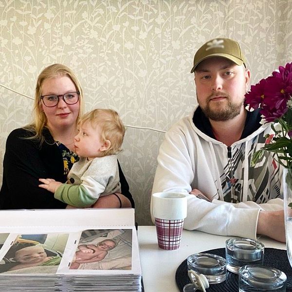 Nyfödd bebis på sjukhus med lakan omkring sig, skadad efter att ha blivit attackerad av hund – två föräldrar i ett kök i Kristinehamn med sin son Liam i famnen