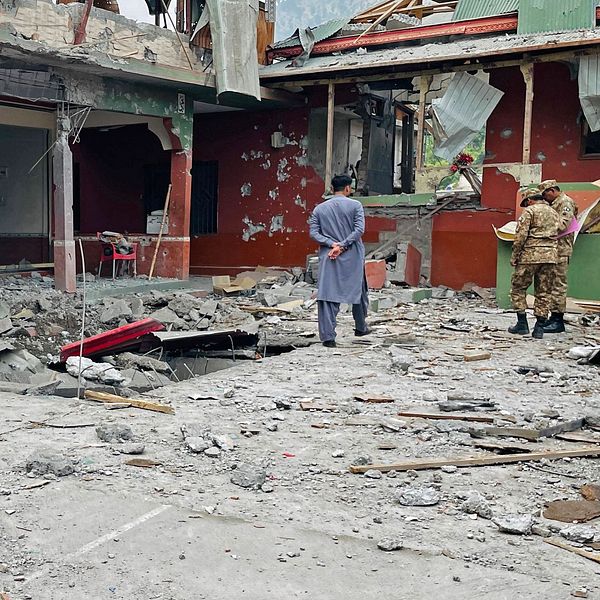Två personer inspekterar raserade rester efter en explosion i ett kraftigt skadat hus.