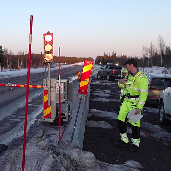 En bomvakt står vid en nedfälld bom på E10 i Gällivare då det ska sprängas i området.