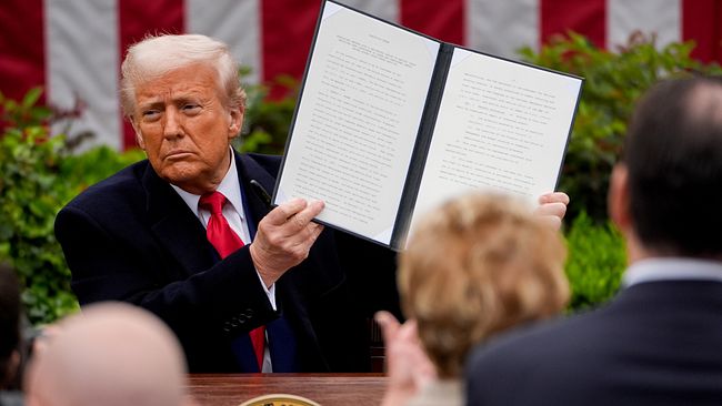 Donald Trump, USA:s president, håller upp officiellt dokument vid talarstol med en sigill. Trump har inför tullar mot en rad länder i ett stort tullpaket.