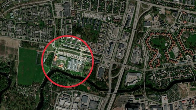 Satellitbild över en stadsmiljö med ett område inringat i rött för att markera ett specifikt område. Området inkluderar byggnader, vägar och grönområden.