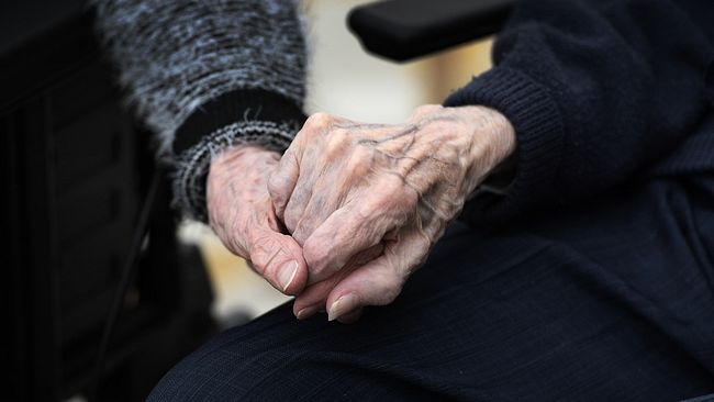 Två personer håller varandra i handen på äldreboende.
