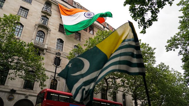 Indiens och Kashmirs flaggor vajande framför ett stenhus och en röd dubbeldäckare.