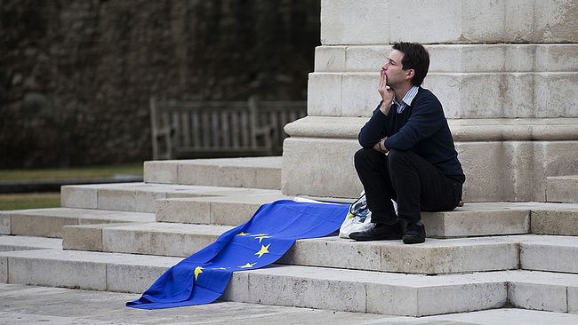 En brittisk man sitter utanför parlamentet med en EU-flagga bredvid sig.