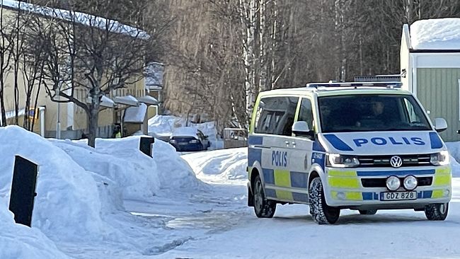 En polisbil står parkerad längs en snötäckt gata i ett bostadsområde i Malå kommun. I bakgrunden syns en gul och en grön fastighet.