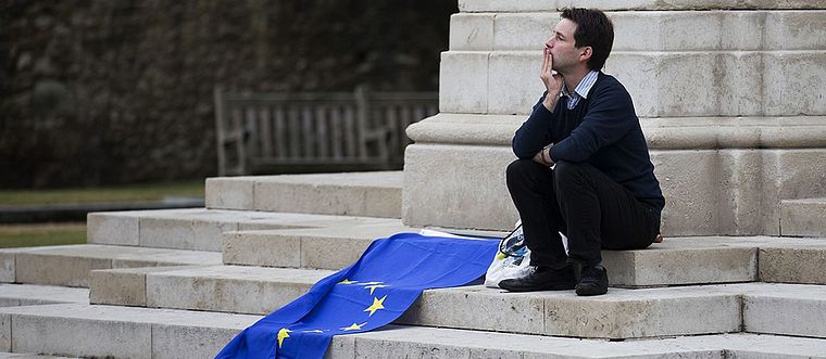 En brittisk man sitter utanför parlamentet med en EU-flagga bredvid sig.