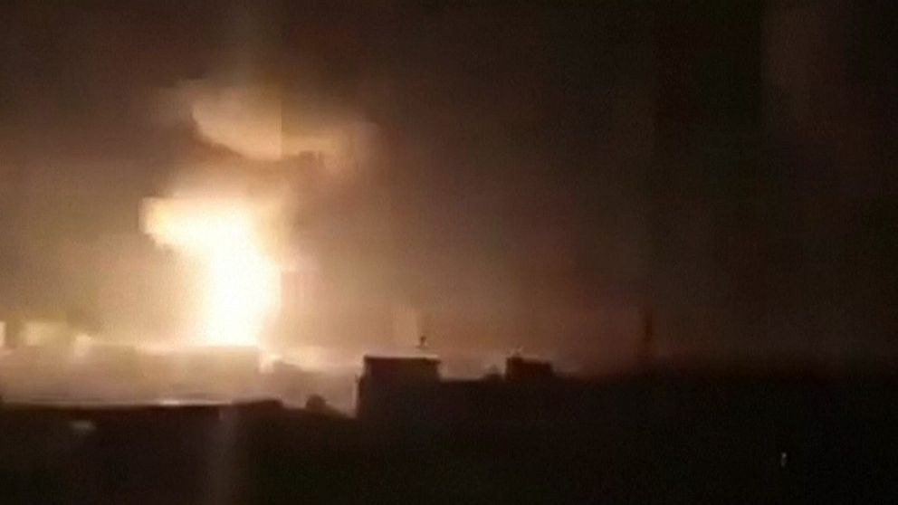 Stor explosion lyser upp natthimlen ovanför mörka byggnader i stadslandskap.