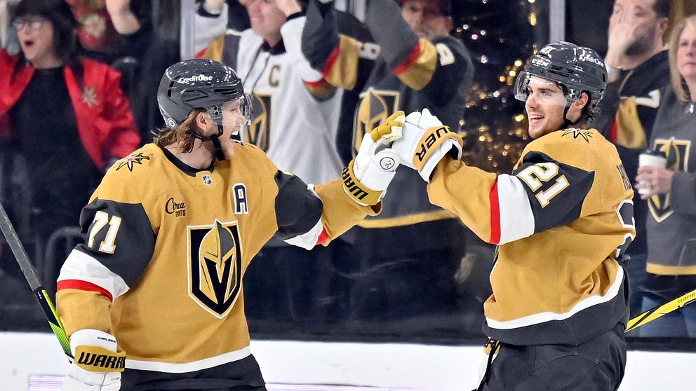 Två spelare från Vegas Golden Knights firar en målscoring under en NHL-match, omgivna av glada fans i bakgrunden. Den ena spelaren bär nummer 71 och en C på sin tröja, vilket indikerar att han är lagkapten, medan den andra har nummer 21.