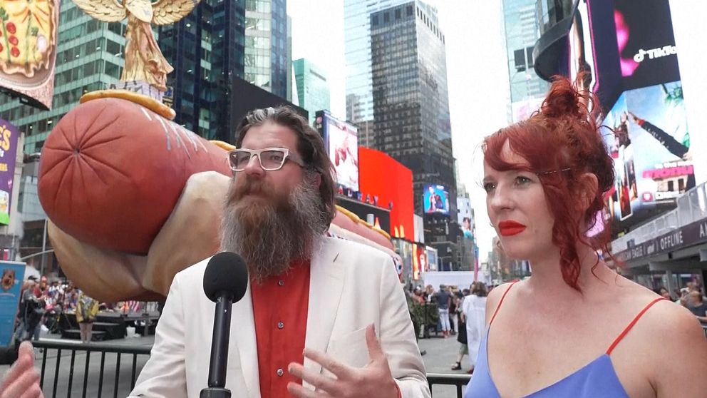 Man med basketboll talar vid mikrofon på Times Square, bredvid kvinna i blå klänning