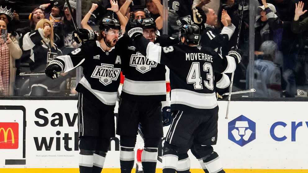 Spelare från Los Angeles Kings firar ett mål på isen, omgivna av entusiastiska fans som jublar i bakgrunden.
