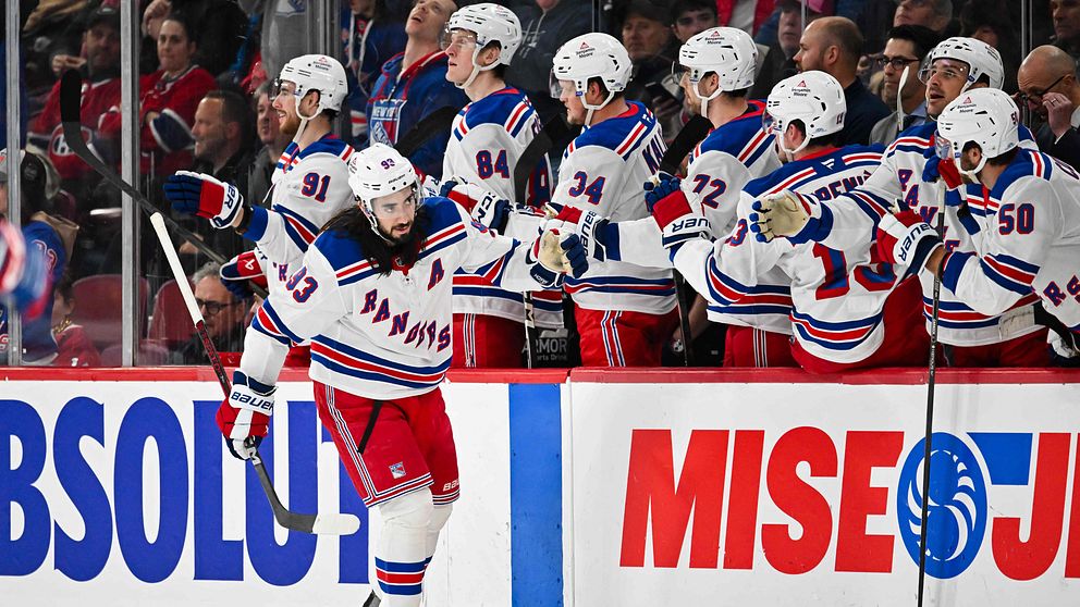 En spelare från New York Rangers firar ett mål och gestikulerar mot bänken, där lagkamraterna entusiastiskt hejar och visar stöd, under en match i NHL.