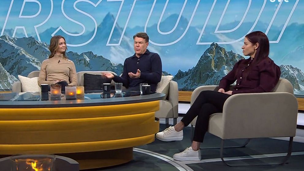 Tre personer sitter i en studiorym med bergslandskap som bakgrund. De samtalar kring ett bord med levande ljusdekorationer.
