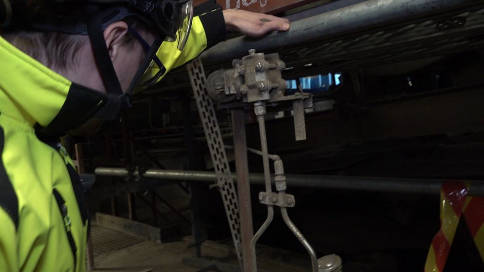 En person i gul arbetsjacka undersöker en ventil eller ventilationsutrustning i en industrimiljö.
