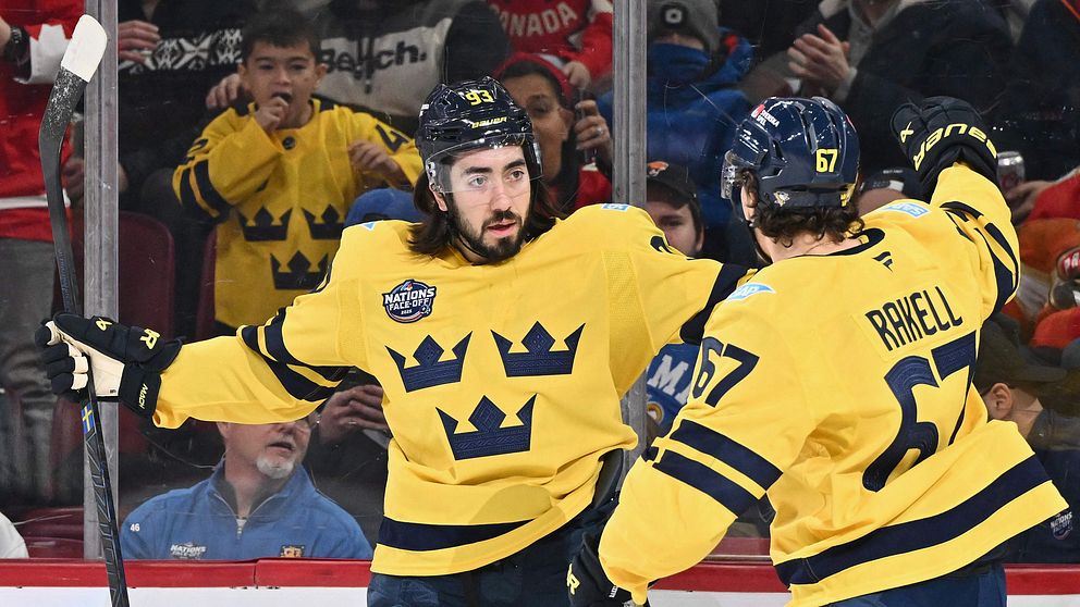 Två svenska ishockeyspelare i gula tröjor firar ett mål på isen. En av spelarna har namnet ”Grell” och nummer 57 på ryggen. Publiken syns i bakgrunden.